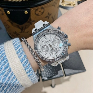 Close-up of silver rhinestone-set bezel watch with white rubber strap on a wrist