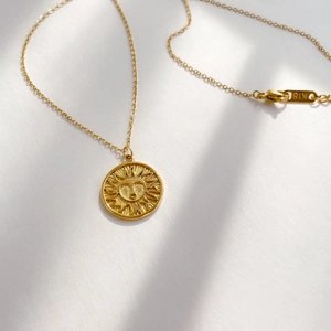 Detailed close-up of K18 engraved clasp on a gold sun pendant necklace with cross chain