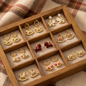 Close-up of pearl earrings with Pegasus and rocking horse motifs in a wooden jewelry box