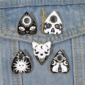 Detailed close-up of dark gothic enamel pins with cat and skull designs on denim fabric