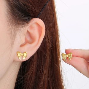 Gros plan d'une boucle d'oreille nœud dorée en acier inoxydable portée à l'oreille