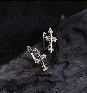 Macro shot of retro silver cross earrings with engraved details on dark wood background