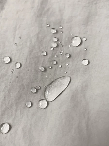 Close-up of waterproof light gray nylon fabric showing water droplets on crossbody bag