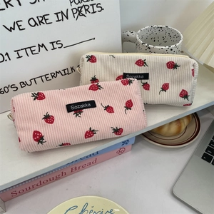 Detail showing pink and off-white corduroy strawberry pencil cases on a styled desk
