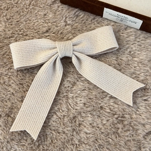 Close-up of cream knit bow hair clip featuring fine vertical ribbing and swallowtail design