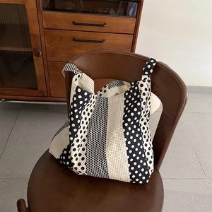 Dettaglio della borsa tote in tela a pois bianchi e neri appesa a una sedia in legno