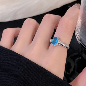 Close-up of a silver ring with a blue oval gemstone and textured rope band on a hand