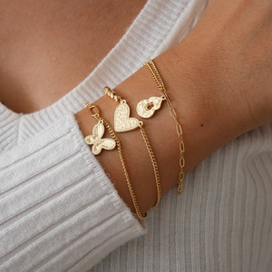 Close-up of three layered gold charm bracelets with butterfly, heart and lock pendants