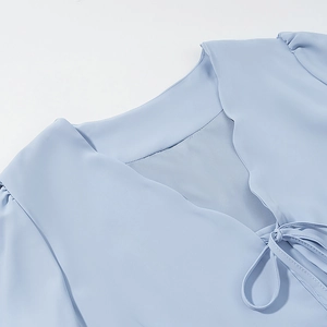 Detail of light blue V-neck top with wavy ruffled edges and elegant tie-up ribbon design