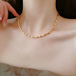 Close-up of asymmetric necklace featuring white pearls and golden cylindrical metal links