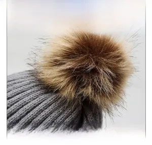 Detail view of grey knit beanie featuring a soft brown faux fur pom pom on top