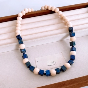 Close-up of vintage beaded necklace with cream round beads and blue square beads on tray