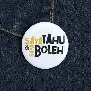 Macro shot of a round tin badge with SAYA TAHU & SAYA BOLEH text on denim fabric