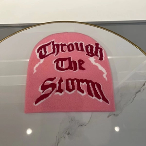 Detail of pink knitted beanie featuring Gothic 'Through The Storm' text on marble surface