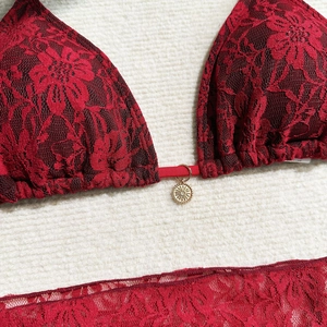 Macro detail of red lace bikini featuring 3D floral textures and a gold sun pendant charm