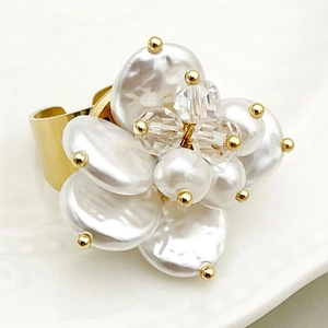 Macro detail of a gold flower ring featuring baroque pearls and a crystal center on a tray