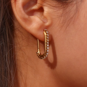 Close-up of gold U-shaped earrings with white pavé-set stones worn by a fashion model