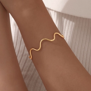 Minimalist wavy gold stainless steel open bangle bracelet worn on a female wrist