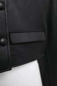 Detailed close-up of premium black leather jacket showing pocket seams and round buttons