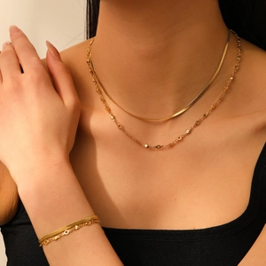 Gros plan sur un ensemble collier et bracelet double couche en maille serpent dorée sur modèle