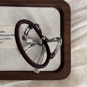 Close-up of a silver hollow bow pendant with S925 engraving on a dark brown hair tie