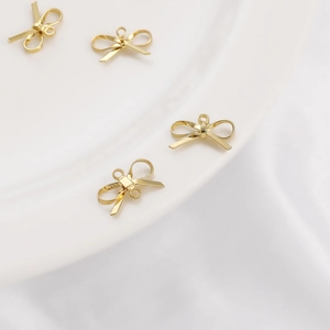 Set of four 14K gold-plated bow pendants for DIY jewelry on white silk fabric background