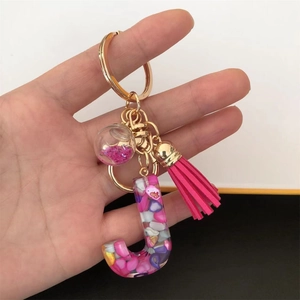 Macro detail of resin letter J keychain with pink sequins, colorful stones and tassel