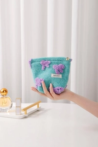 Close-up of mint green plush pouch featuring purple floral applique and flower zipper pull