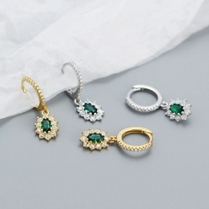 Macro shot of gold and silver leverback earrings with oval emerald green zircon pendants