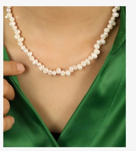 Detail of elegant freshwater pearl necklace worn by a model over a dark green silk shirt