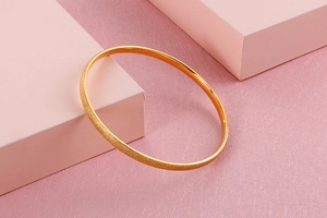 Detail of gold titanium steel bangle with matte sandblasted finish on a pink cube stand