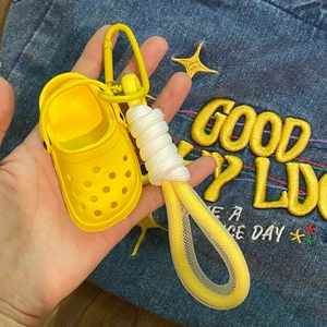 Detail of yellow mini clog shoe keychain with braided rope strap on blue denim background