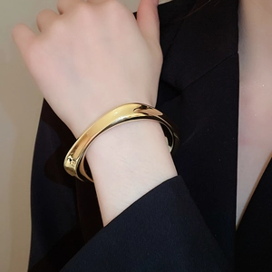 Gros plan d'un large bracelet manchette doré poli porté sur une manche de costume sombre