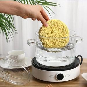 Transparent glass cooking pot with dual handles on a white electric heater on wood table