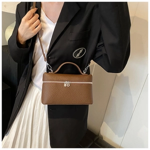 Close-up of brown litchi pattern leather handbag paired with a black blazer and white skirt