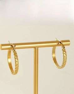 Detailed view of gold braided hoop earrings with secure clasp on a minimalist display stand