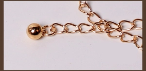Detail of a minimalist gold metal chain with round corn bead ornament and hook