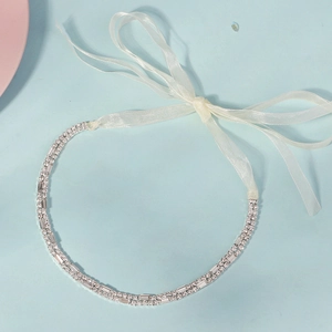 Detail of silver rhinestone bridal headband with white silk ribbon on a blue surface