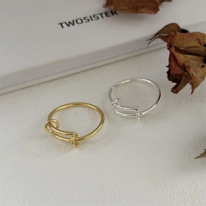 Minimalist knot design rings in gold and silver colors displayed on a textured white surface
