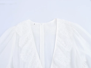 Détail du col en V robe blanche avec bordure en dentelle et étiquette sur tissu mousseline