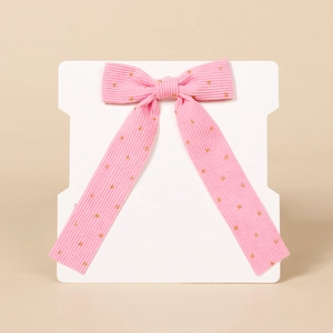 Close-up of pink corduroy bow hair clip with gold polka dots on white display card