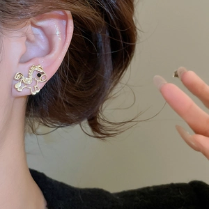 Detail of a hollow gold horse stud earring with black bead eye worn by a model