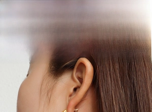 Detailed view of model wearing gold-plated twisted rope hoop earrings with polished finish