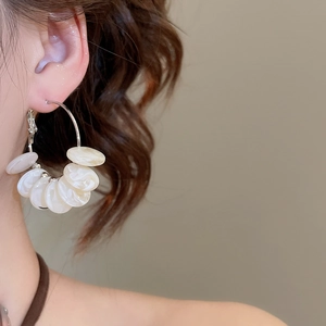 Close-up of a silver needle hoop earring with white resin charms worn by a model