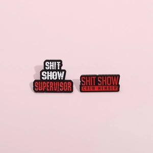 Detail of enamel pins featuring Shit Show Supervisor and Crew Member text on red background