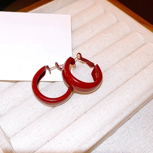 Close-up of red enamel C-shaped hoop earrings on a textured white jewelry display