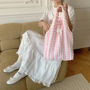 Detail of pink and white striped bubble texture tote bag on a white lace dress background