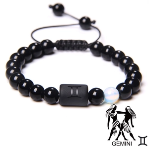 Detail of Gemini zodiac braided bracelet featuring black matte beads and engraved symbol