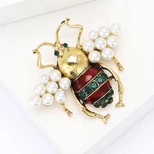 Vintage gold bee brooch with pearl wings and red-green striped enamel on white background