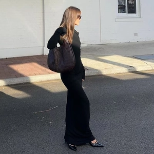 Détail d'une robe longue noire ajustée avec un grand sac porté épaule marron tressé